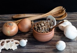 Boiled buckwheat in a pot, onion, fresh mushrooms and wooden spoons on the table