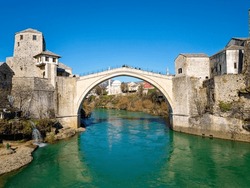 Aerial drone view of the Old Bridge in Mostar city in Bosnia and Herzegovina during sunny day. Blue turquoise colors of Neretva river. Unesco World Heritage Site. People walking over the bridge.