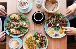 Different colorful meals for breakfast or lunch time on a plate with cutlery on woman's hands. Fried eggs, omelette, bruschetta and sausage on a wooden teble in restaurant. Flat lay top view.