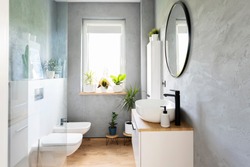 Modern bathroom with grey wall, white furniture and wooden tiles on a floor. Bright interior with window, mirror and stylish washbasin. Minimalism and scandinavian design of washroom.