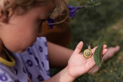 Little girl with snail on a hand outdoor. Mindfulness and focus on wild nature. Macro. Autism child and childhood.