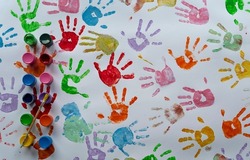 Colorful hand prints with paints and watercolor on white paper. Imprints of little child during fun, sensory play and education in kindergarten. Many hands in different color. Top view.