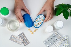 Hand with pills and pillboxes. Top view of six day pill box with pills. Blue pill-box over light marble table. Open pill box and open boxes with pills or vitamins. Pill box for senior patient