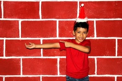 Latin brown boy very happy with the arrival of Christmas wears a red hat in front of a brick wall

