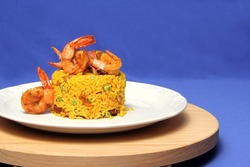 Paella rice is a traditional cuisine recipe from the city of Valencia Spain prepared with saffron, seafood, shrimp, vegetables served on a white plate on a blue background