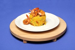 Paella rice is a traditional cuisine recipe from the city of Valencia Spain prepared with saffron, seafood, shrimp, vegetables served on a white plate on a blue background