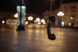 Hanging Public telephone at night , ear phone,  pay phone. hanging phone.
Feelings - separation, emptiness, loneliness, resentment. bokeh background
