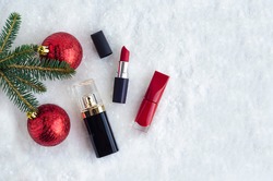 decorative luxury cosmetics, red lipstick, nail polish, perfume under spruce branch with balls in the snow. gifts for women, girl for new year. Christmas sale. copy space, place for text. top view