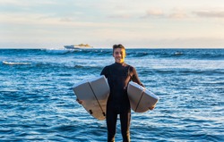 Young surfer comes out of the water with the board broken in half. Handsome guy with wetsuit. Horizon over the water and incoming ship.
