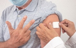 Doctor after injecting a 70-year-old man with booster the third dose of the coronavirus vaccine covid-19. The man shows the number three with his hand. Concept of against new omicron variant.
