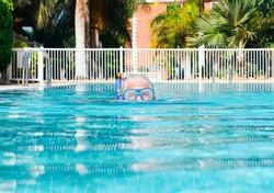 Senior adult active man swimming in the outdoors swimming pool wearing diving mask, enjoying sport, relax and healthy lifestyle. Elderly grandfather looking at camera. Copy space