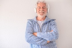 Senior bearded man over isolated white background listening to music with headphones. Smiling elder white haired man enjoying music
