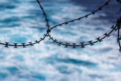 Close up view of razor wire fortification at ship's stern. Anti piracy protection. HRA, High Risk Areas. Illegal boarding. Ship's wake in background. Selective focus.