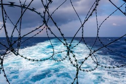 Close up view of ship's stern fortified with razor wire. Anti piracy protection. HRA, High Risk Areas. Illegal boarding. Ship's wake in background. Selective focus.