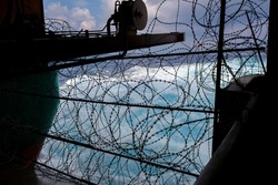 Ship's stern fortified with razor wire. Anti piracy protection is mounted before entering (HRA) Piracy High Risk Areas to prevent illegal boarding. Ship's wake in background.