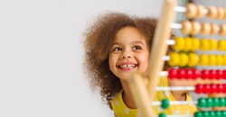 A Black student in a yellow dress laughs brightly behind a colored abacus in an elementary school classroom