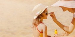 Mom carefully smears her child's face with protective cream on the beach. Skin care. Protection from the sun. Sunscreen for children.