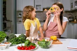 mom and her daughter playfully cook healthy and proper food from fresh vegetables and herbs.The girl makes herself a kind of glasses from pepper circles