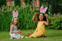 two girls during Easter egg hunt and putting Easter eggs in baskets