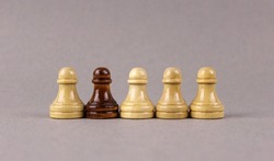One black chess pawn among whites pawns on gray background