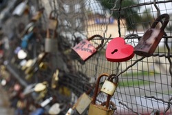 Close up of red heart-shaped love lock hanging on a bridge on the blurry background of other locks. Valentine's Day and Love concept.