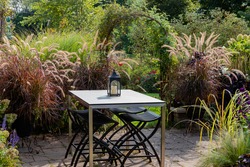 A contemporary  White rectangular ceramic  dining garden table is the focal point of this  relaxing naturalized prairier garden of ornamental grasses, pennisetum and miscanthus