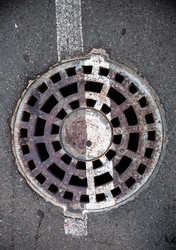 Manhole with metal cover in asphalt with white road marking line on it.