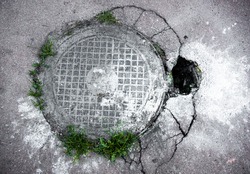 Manhole in cracked asphalt surface with a big hole near the cover