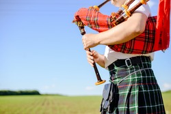 Male playing Scottish traditional pipes on green summer outdoors background, closeup image 