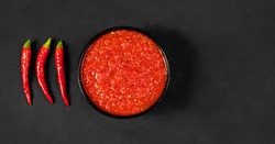 Adjika on a black background. Hot chili peppers harissa sauce. Homemade rose harissa in a bowl. Copy space, top view, flat lay.