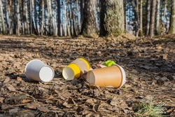 Household garbage left in the forest by tourists. Coffee paper cups, crumpled sheets of paper are scattered on the path. The concept of environmental pollution with household waste.