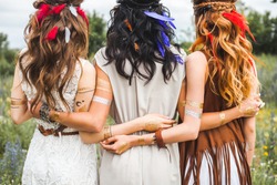 Summer holidays, vacation, travel and people concept - three beautiful hippie girl, photographed from behind, hairstyles, feathers, white dresses, flash tattoo, accessories, Bohemian, Bo-ho Style