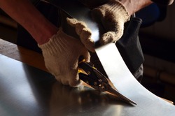 worker cuts a stainless sheet with scissors for metal