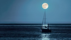 A sailing yacht goes out to sea in the moonlight at night. The moon is on the horizon just above the top of the mast. The red light mast is located directly behind the sailboat at the port entrance.