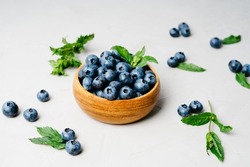 Blueberries are scattered on a gray table. Berries on a gray textured background. Top view of a bowl of blueberries. Fresh mint. The concept of healthy eating and nutrition.