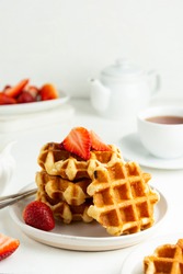 Delicious breakfast. Belgian waffles with honey and strawberries. Cup of tea white wooden background