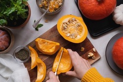 Fresh pumpkin. Cutting pumpkin in slices on cutting board, female hands preparring autumn foods. Baked squash or butternut, top view.