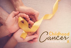 adult and child hands holding yellow gold ribbon, Childhood cancer Awareness month