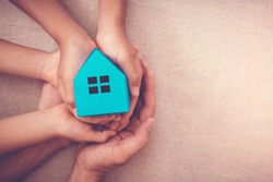 Adult and child hands holding paper house, family home, homeless housing and home protecting insurance concept, international day of families, foster home care, family day care, social distancing