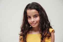 urban lifestyle portrait of a confident and gorgeous mixed race child face, multiethnic tween preteen teen girl with beautiful curly hair wearing yellow summer dress, smiling at camera, youth day