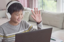 Preteen tween teen Asian boy making facetime video calling with laptop at home, using zoom  online virtual class , social distancing ,homeschooling,learning remotely during covid coronavirus pandemic