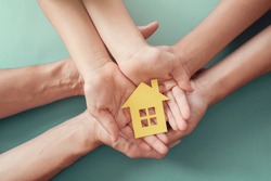 Adult and child hands holding paper house, family home, homeless housing and home protecting insurance concept, international day of families, foster home care, homeschooling, social distancing 