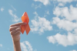 Hands holding orange Ribbon over blue sky,  Leukemia cancer and Multiple sclerosis, COPD and ADHD awareness, world kidney day