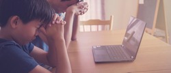 Preteen boy praying with father parent with laptop, family and kids worship online together at home, streaming online church service, social distancing concept