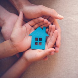 Adult and child hands holding paper house, family home, homeless housing and home protecting insurance concept, international day of families, foster home care, family day care, social distancing