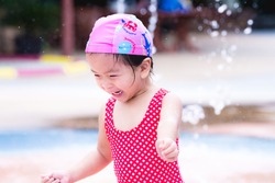 Happy Asian child girl playing water. Laughing children. Kids run around in the fountain. Baby was wearing a pink swim cap and a red bathing suit with a diamond pattern. Toddler aged 3 year old.