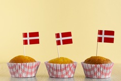 Homemade cupcake with Denmark flag on beige wood background. Holiday Independence Day. Danish flag decorates cakes.