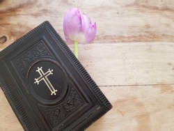 An ancient Danish hymnbook (Psalmer) with prayers and verses to sing in church or at home laying on a wooden vintage table with a single purple tulip. Communion, church, hope concept - space for text
