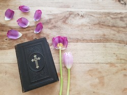 An ancient Danish hymnbook (Psalmer) with prayers and verses. Laying on a wooden table with pink and purple tulips and tulip petals. Communion, church, hope concept - space for text