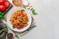 Penne pasta with bolognese sauce, fresh tomatoes and basil on a gray background. Top view, copy space.
